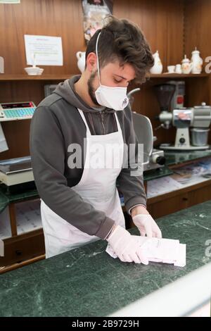 Avetrana, Italien, - Marth 19, 2020. Der Verkäufer serviert einem Kunden einen in Scheiben geschnittenen Schinken, trägt während der Coronavirus Epidemie eine medizinische Maske und Handschuhe. Stockfoto