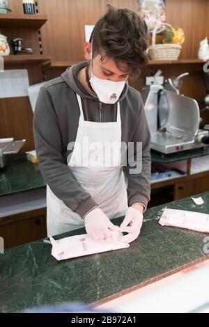 Avetrana, Italien, - Marth 19, 2020. Der Verkäufer serviert einem Kunden einen in Scheiben geschnittenen Schinken, trägt während der Coronavirus Epidemie eine medizinische Maske und Handschuhe. Stockfoto