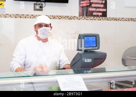 Avetrana, Italien, - Marth 19, 2020. Der Verkäufer serviert einem Kunden Fleisch, trägt medizinische Maske und Handschuhe Schutz während Coronavirus Epidemie. Schopp Stockfoto