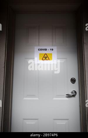 Eine selbstisolierende Residenz mit einem Quarantäneschild an der Vordertür, das vor dem Covid-19-Virus warnt. Stockfoto