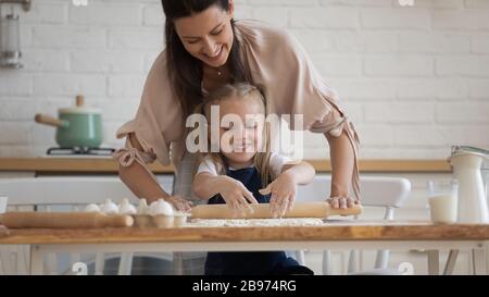 Lächelnde Mutter, die kleine Tochter beigebracht hat, Teig zu machen Stockfoto