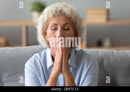 Ältere Gläubige beten zu Hause mit den Händen im Gebet Stockfoto
