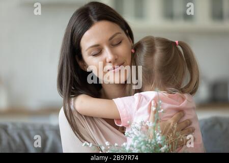 Kleine Tochter umarmen junge Mutter mit Blumen Stockfoto