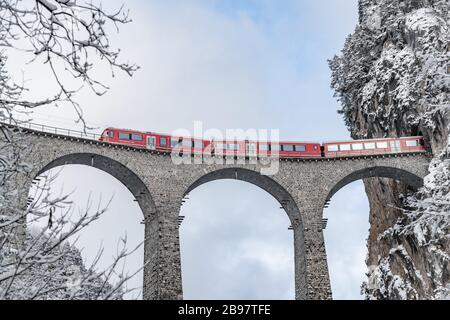 Der Landwasser-Viadukt mit berühmtem roten Zug zur Winterzeit, Wahrzeichen der Schweiz, schneit, Glacier Express Stockfoto