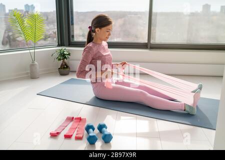 Home Workout mit Widerstand Band Fitness Asiatische Frau Training zurück Muskeln mit Ruderarmbewegung mit Gummibändern beim Yoga Übungen für den Mattenboden Stockfoto
