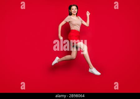 Ganzkörperprofil Foto von Pretty Lady Jump hoch jubelnd hetzende Sommer letzte Saison Verkaufspreise Shopper tragen Freizeit gestreiftes T-Shirt roter Rock Stockfoto