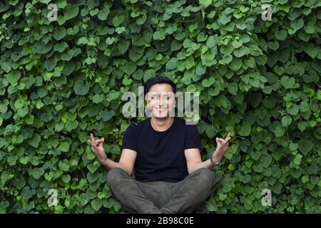Lächelnder asiatischer junger Mann in schwarzem T-Shirt, das Yoga posiert Stockfoto