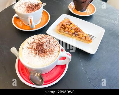 Bistrotisch aus schwarzem Stein mit Tassen Cappuccino und Gebäck. Studio Foto Stockfoto