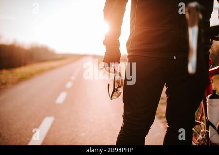 Der Biker steht auf der Straße und hält seine Brille in der Hand Stockfoto