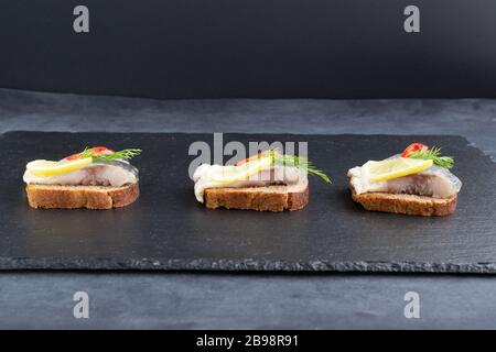 Sandwiches mit eingelegtem Hering mit Zitrone, Chili und Dill. Gesunde Ernährung. Schwarzer Hintergrund. Stockfoto