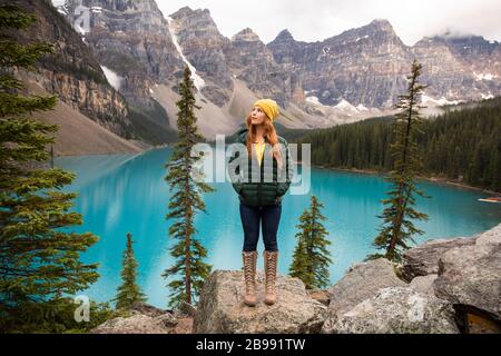 Rothaariges Mädchen in gelber Mütze und Stiefeln mit Moränensee banff im Hintergrund Stockfoto
