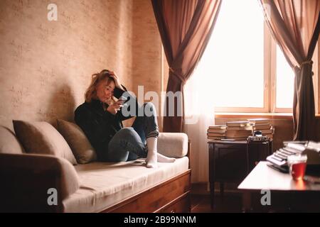 Junge traurige betonte Frau, die mit dem Smartphone unterwegs auf dem Sofa zu Hause sitzt Stockfoto