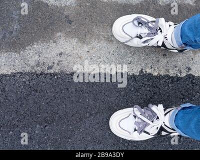 Asphaltstraßenreparaturkonzept. Eine Person steht auf den alten grauen und neuen dunkelgrauen Asphaltflächen im Freien Stockfoto
