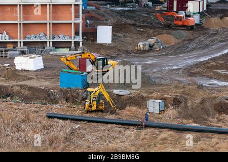 Blick auf Baumaschinen, Bagger auf Baustelle, Räumgebiet und Verlegerohre. Mehrstöckiges Gebäude im Bau o Stockfoto