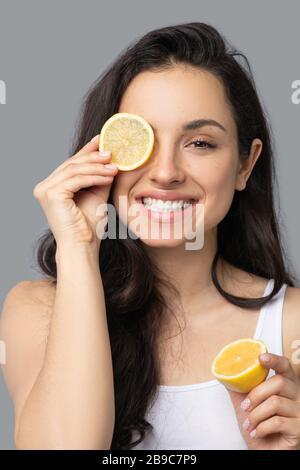 Schönes dunkelhaariges Mädchen, das eine Orange in den Händen hält und ein Auge schließt Stockfoto