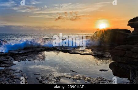 Heiße aufgehende Sonne über Horizont und Sandsteinfelsen von Turimetta, dem Kopf der Nordstrände von Sydney. Stockfoto