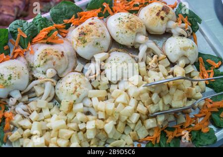 Ganze gegrillte Tintenfische mit Bratkartoffeln. Marinade mit Olivenöl extra vergine Öl, gehacktem Knoblauch und Petersilie in einer Aluminiumschale für Selbstbedienung oder Stockfoto