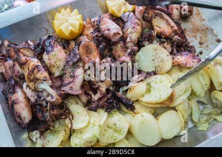 Baby Tintenfisch vom Grill mit Bratkartoffeln, Zitrone, mariniert mit Olivenöl, Knoblauch und Petersilie in einer Aluminiumschale für Selbst-Servic Stockfoto