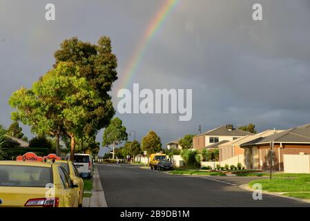Dunkle Regenwolken und Regenbogen in der Suburban Street mit Autos und Häusern Stockfoto