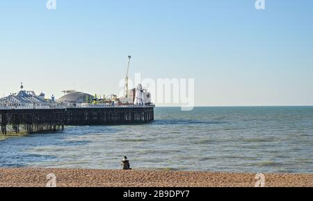 Brighton UK 24. März 2020 - EINE Person sitzt allein am Brighton Strand an einem schönen sonnigen Morgen, während die neuen staatlichen Einschränkungen während der Coronavirus COVID-19-Pandemie-Krise kommen. Kredit: Simon Dack / Alamy Live News Stockfoto