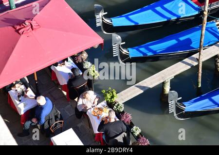 Blick von oben auf die Gäste, die eine Mahlzeit auf einer Terrasse am Canal Grande mit Gondeln genießen Stockfoto