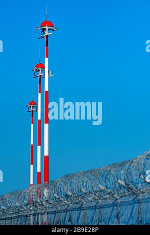 Zaun mit Stacheldraht und Reihe der Flughafenlampenpfosten mit wechselndem rot-weißen Anstrich gegen blauen Himmel, Sicherheitskonzept Stockfoto