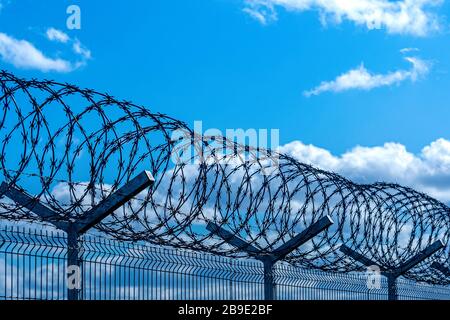 Zaun mit Stacheldraht gegen blauen Himmel mit Wolken, Sicherheitskonzept Stockfoto