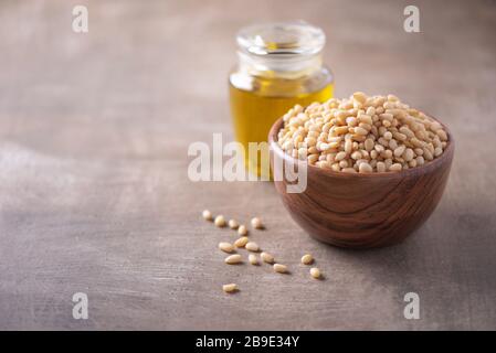 Rohe Pinienkerne in Holzschale und Pinienknüsse in Flasche auf strukturiertem Holzhintergrund. Kopierbereich. Superfood, veganes, vegetarisches Speisekonzept. M Stockfoto