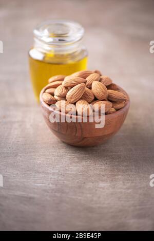 Mandelmuttern in Holzschale und Mandelöl in Flasche auf strukturiertem Holzhintergrund. Kopierbereich. Superfood, veganes, vegetarisches Speisekonzept. Makro von Almon Stockfoto