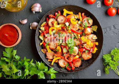 Scheiben von gebratenem Gemüse mit Würstchen und Gewürzen in der Pfanne. Ansicht von oben, flach Stockfoto