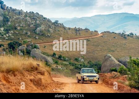 Altes Auto, das auf roter, schmutzige Straße in erstaunlicher Landschaft von Eswatini fährt Stockfoto