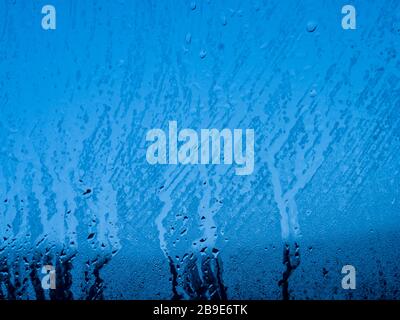 Kondenswasser fällt auf das blaue Glasfenster. Regen. Abstrakte Hintergrundtextur. Stockfoto