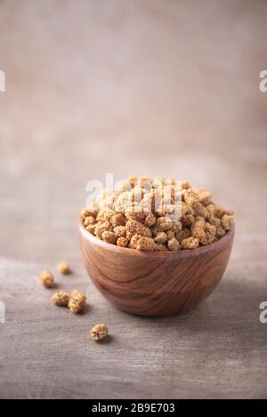 Weiße getrocknete Maulbeere in Holzschale auf strukturiertem Holzhintergrund. Kopierbereich. Superfood, veganes, vegetarisches Speisekonzept. Makro der Maulbeeren, sel Stockfoto