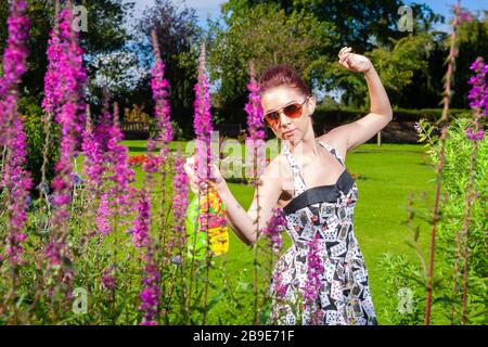 Eine attraktive junge Frau, die an einem Sommertag in Schottland ein Sommerkleid trägt und Pflanzen sprüht. Stockfoto