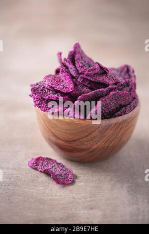 Getrocknete Scheiben von rosafarbenen Drachenfrüchten, Pitaya in Holzschale auf strukturiertem Holzhintergrund. Kopierbereich. Superfood, veganes, vegetarisches Speisekonzept. Makro von Stockfoto