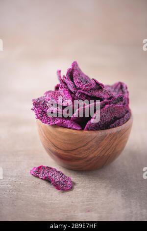 Getrocknete Scheiben von rosafarbenen Drachenfrüchten, Pitaya in Holzschale auf strukturiertem Holzhintergrund. Kopierbereich. Superfood, veganes, vegetarisches Speisekonzept. Makro von Stockfoto