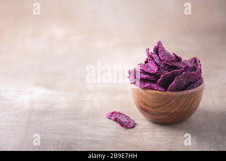 Getrocknete Scheiben von rosafarbenen Drachenfrüchten, Pitaya in Holzschale auf strukturiertem Holzhintergrund. Kopierbereich. Superfood, veganes, vegetarisches Speisekonzept. Makro von Stockfoto