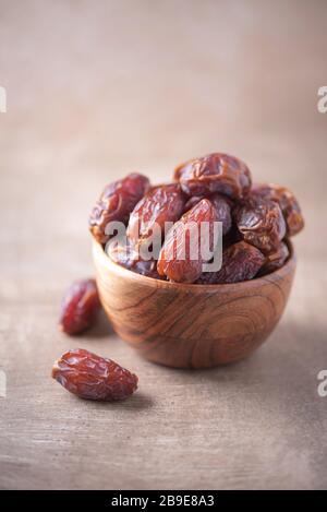 Trockendatierobst in Holzschale auf strukturiertem Holzhintergrund. Kopierbereich. Superfood, veganes, vegetarisches Speisekonzept. Makro der Datenstruktur, selektiv Stockfoto