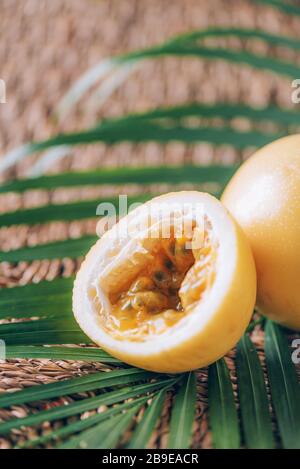 Gelbe Maracuya mit Palmblättern auf Rattanhintergrund. Kopierbereich. Passionsfrucht. Banner für kreatives Design. Sommerzeit. Tropische Reise, exotische Früchte. Stockfoto
