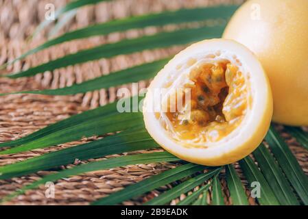 Gelbe Maracuya mit Palmblättern auf Rattanhintergrund. Kopierbereich. Passionsfrucht. Banner für kreatives Design. Sommerzeit. Tropische Reise, exotische Früchte. Stockfoto