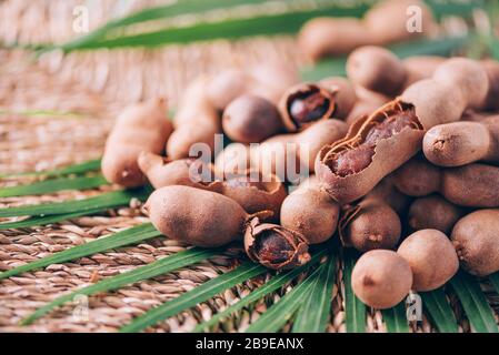 Süße reife Tamarinde mit Palmblättern auf Rattanhintergrund. Kopierbereich. Tropische Reise, exotische Früchte. Veganes und vegetarisches Konzept. Stockfoto