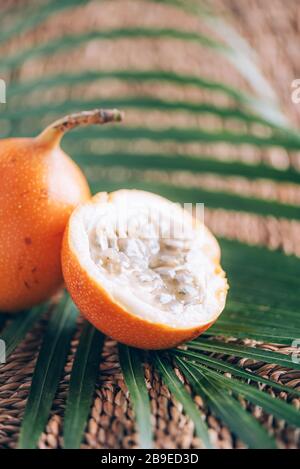 Süße Granadilla oder Granadia mit Palmblättern auf Rattanhintergrund. Kopierbereich. Banner für kreatives Design. Sommerzeit. Exotische Küche, tropische Obstkonce Stockfoto