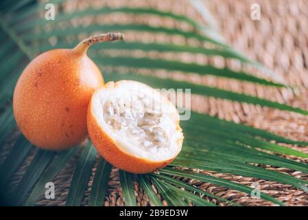 Süße Granadilla oder Granadia mit Palmblättern auf Rattanhintergrund. Kopierbereich. Banner für kreatives Design. Sommerzeit. Exotische Küche, tropische Obstkonce Stockfoto