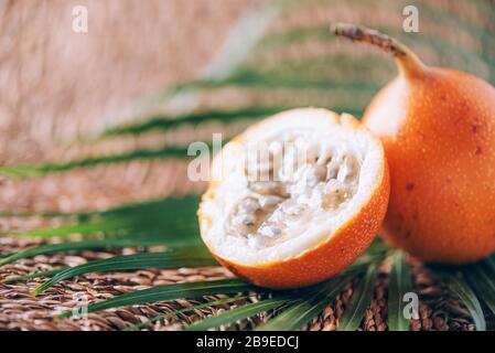Süße Granadilla oder Granadia mit Palmblättern auf Rattanhintergrund. Kopierbereich. Banner für kreatives Design. Sommerzeit. Exotische Küche, tropische Obstkonce Stockfoto
