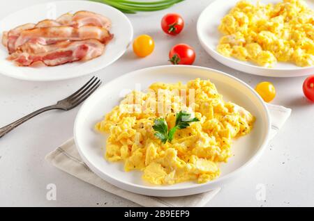 Gesundes Diät-Frühstücks-Konzept. Rührei, Speck und Tomaten über weißem Steingrund Stockfoto