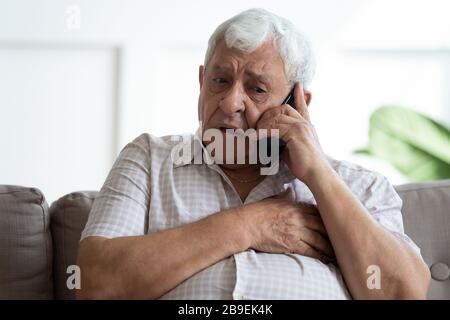 Verärgert den älteren Mann, der die Brust berührt, und ruft einen Notfall an, Herzinfarkt Stockfoto