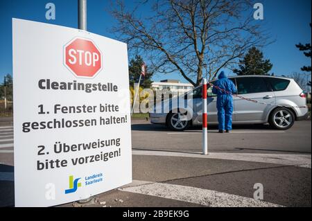 24. März 2020, Saarland, Saarlouis: Eine Frau in einem Schutzanzug überprüft die Überweisungen von Menschen, die zur Einfahrteststation auf dem Parkplatz des Ford-Werks kommen. Dort wurde die Covid-19-Fahrt in Test Saarlouis (CITS) eröffnet, bei der Ärzte einen Schlupf nehmen, um auf das Corona-Virus zu testen. Foto: Oliver Dietze / dpa Stockfoto