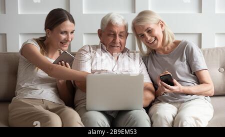 Glückliche ältere Eltern mit Erwachsenentochter, die elektronische Geräte verwenden Stockfoto