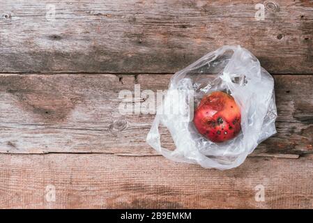 Verdorbener roter apfel in Plastiktüte auf Holzhintergrund. Mülleimer verfaulen Lebensmittel. Draufsicht. Kopierbereich. Morsches Gemüse- und Obstkonzept. Null Stockfoto