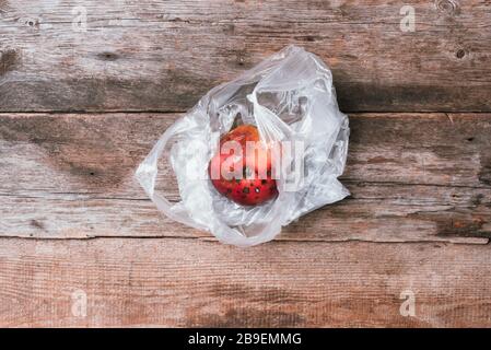 Verdorbener roter apfel in Plastiktüte auf Holzhintergrund. Mülleimer verfaulen Lebensmittel. Draufsicht. Kopierbereich. Morsches Gemüse- und Obstkonzept. Null Stockfoto